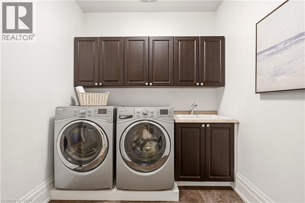 Dedicated laundry area featuring dark wood-finish cabinetry with silver hardware, a built-in sink with a countertop, and durable flooring - 336 Newbold Court, Burlington, ON