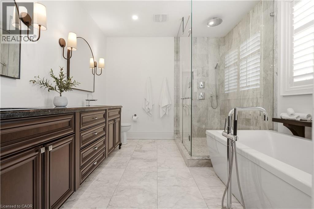 Spacious bathroom featuring a dual vanity with dark wood cabinetry and dark countertops, a large glass-enclosed shower with tile surround, a freestanding soaking tub with floor-mounted faucet, and mar - 336 Newbold Court, Burlington, ON