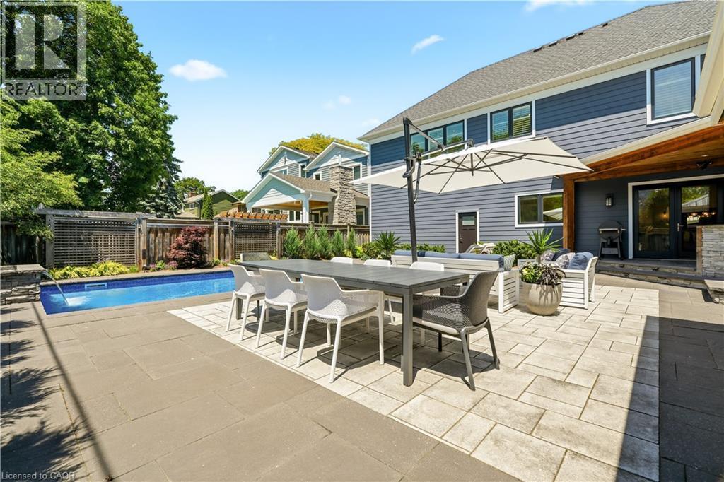 Expansive patio featuring a built-in swimming pool, mixed paver and slab hardscaping, and a wood-beamed covered outdoor area - 336 Newbold Court, Burlington, ON
