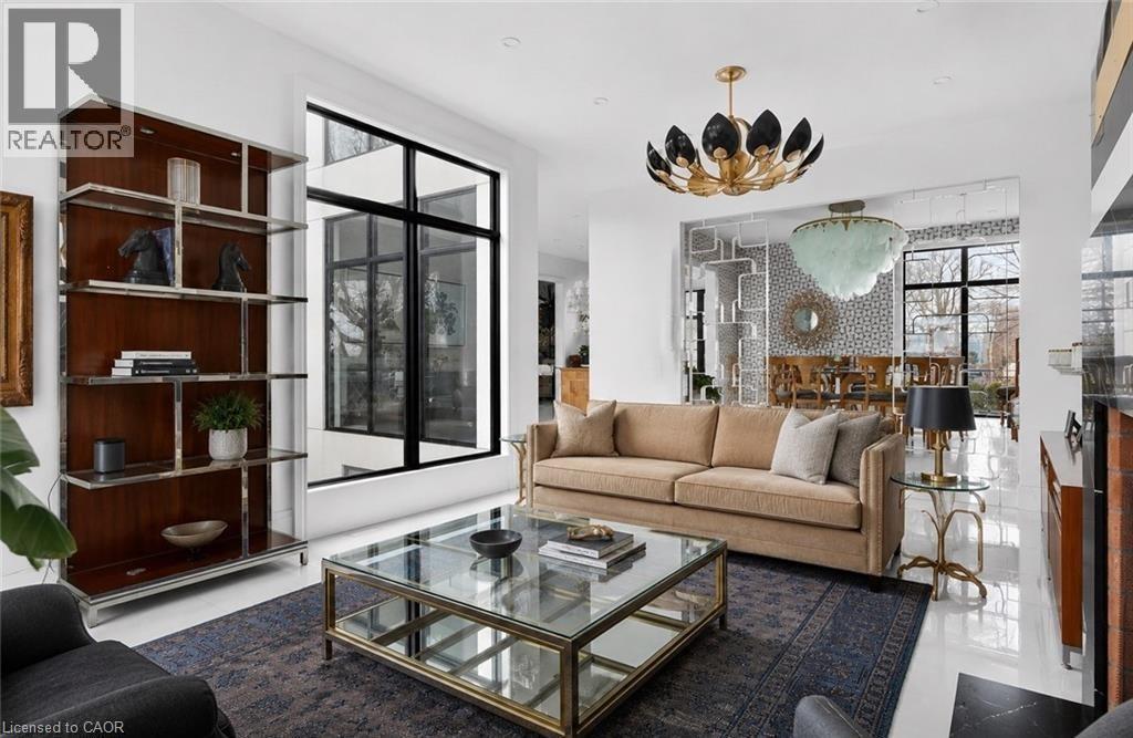 Spacious living area featuring polished white flooring, a built-in shelving unit with wood-finish backing and chrome accents, a full-height window with black frames, and a distinctive overhead light f - 711 Beach Boulevard, Hamilton, ON