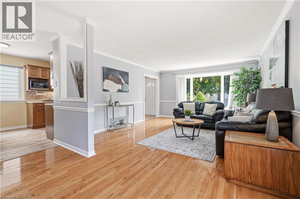 Living area with wood-finish flooring, a broad picture window, light gray walls with chair rail molding, and white crown molding - 4277 Longmoor Drive, Burlington, ON