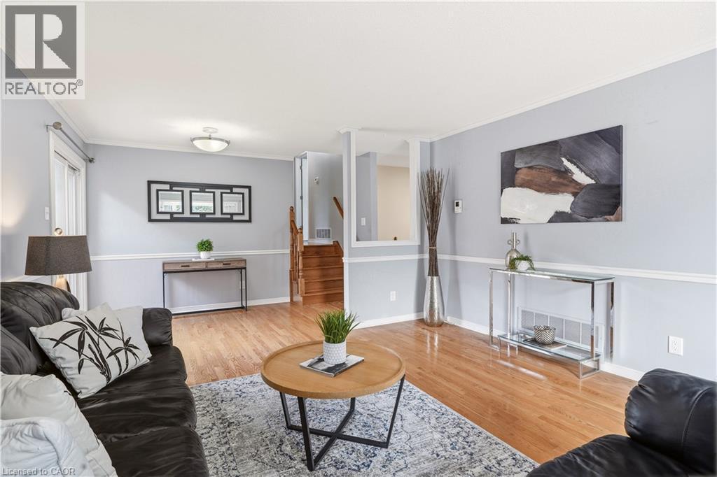 Spacious living area featuring wood-finish flooring, light gray wall tones with white trim, and a built-in staircase with wood risers and handrails - 4277 Longmoor Drive, Burlington, ON