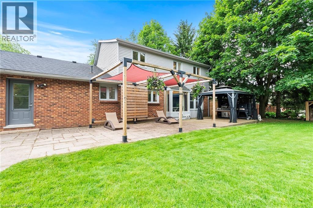 Expansive backyard featuring a stone patio, lush green lawn, pergola with red sunshade, and a freestanding gazebo - 44 Fireside Drive, Hamilton, ON