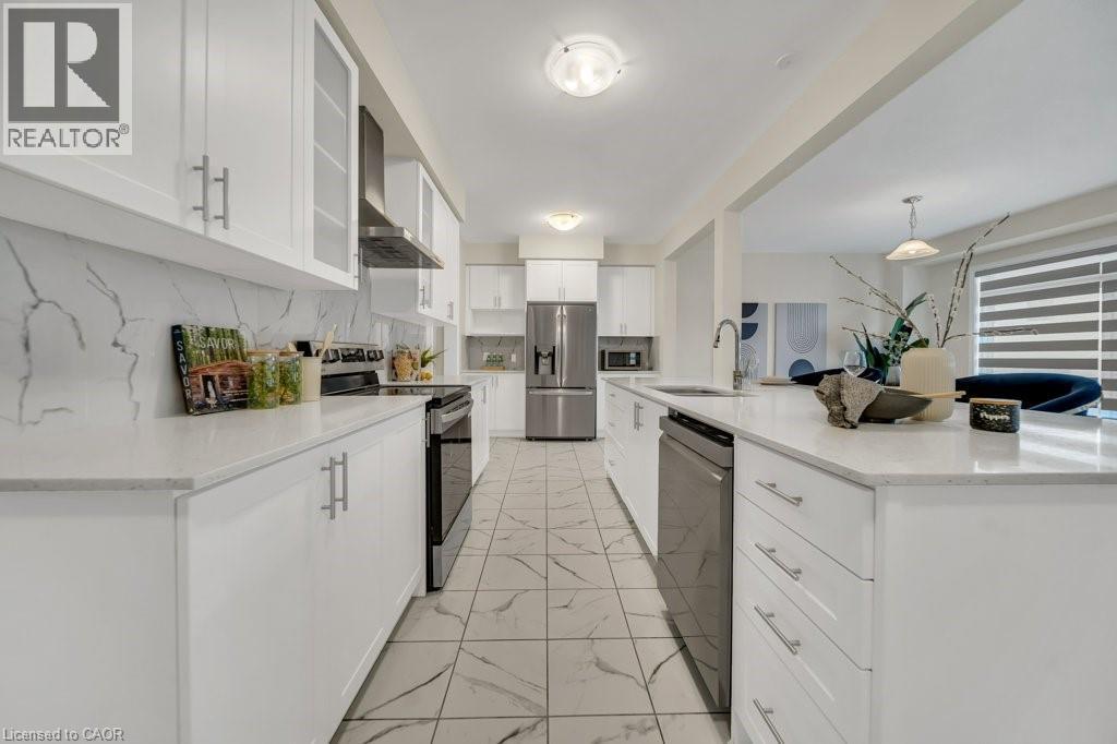 Kitchen featuring appliances with stainless steel finishes, tasteful backsplash, white cabinets, wall chimney range hood, and light marble finish flooring - 285 Broadacre Drive, Kitchener, ON