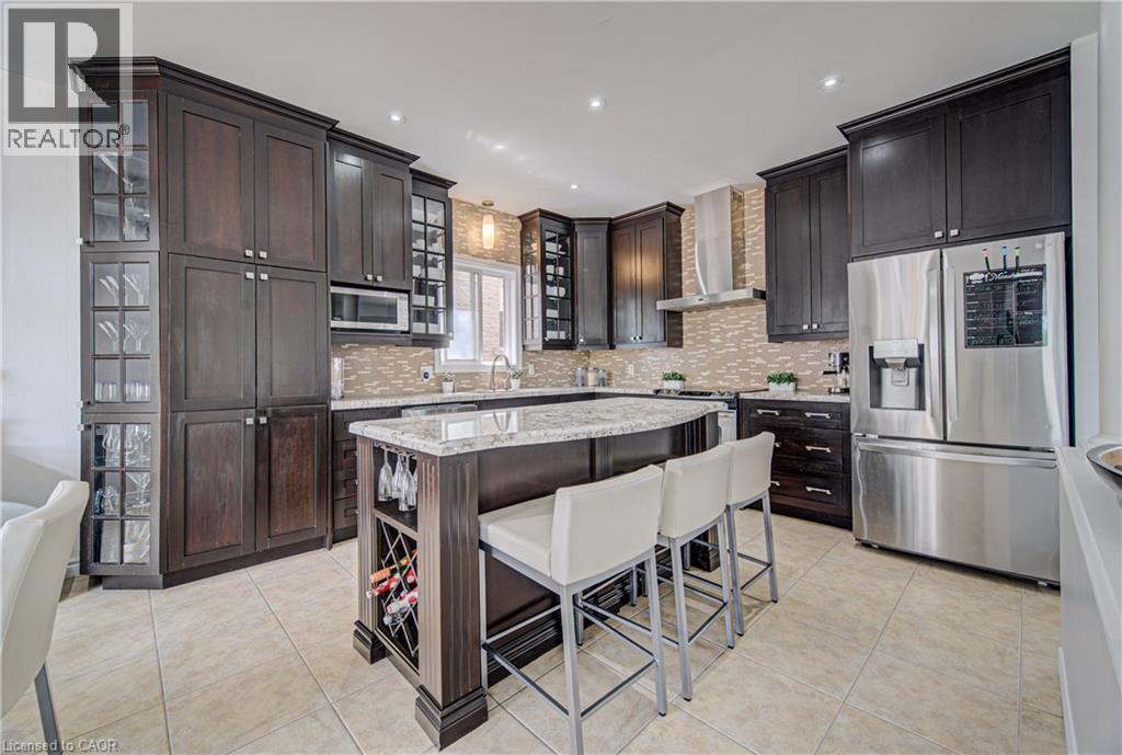 Gourmet kitchen featuring dark wood cabinetry, stainless steel appliances, a tiled backsplash, a central island with integrated wine storage, and light-toned tile flooring - 37 Davinci Boulevard, Hamilton, ON
