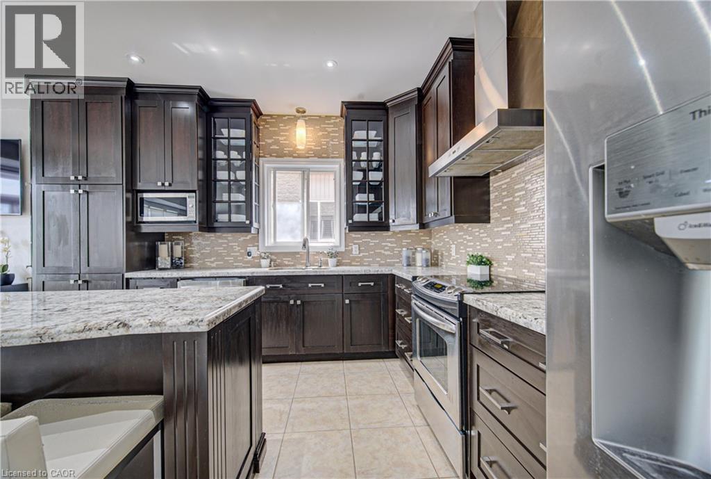Contemporary kitchen featuring dark wood cabinetry, light granite countertops, a mosaic tile backsplash, and stainless steel appliances - 37 Davinci Boulevard, Hamilton, ON