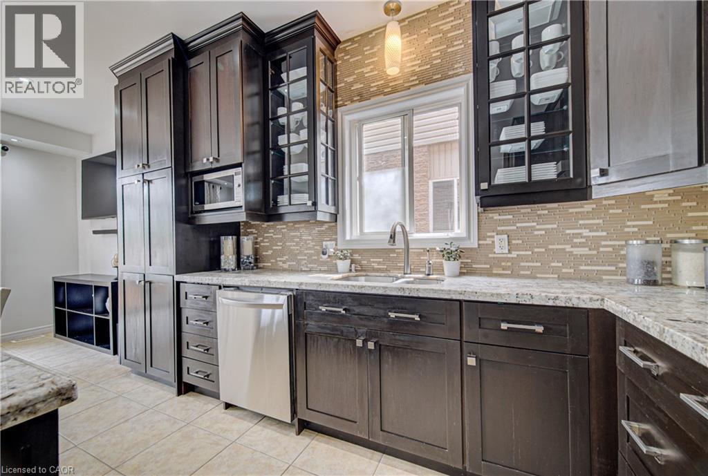 Modern kitchen featuring dark wood-finish cabinetry, light-colored stone countertops, and a full tile backsplash - 37 Davinci Boulevard, Hamilton, ON