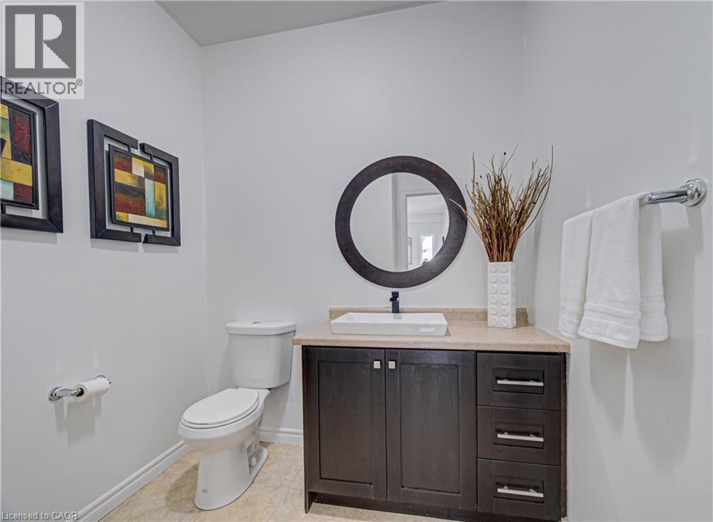 Powder room featuring a dark wood-finish vanity with a light-colored countertop, vessel sink with a black faucet, and a round dark-framed mirror - 37 Davinci Boulevard, Hamilton, ON