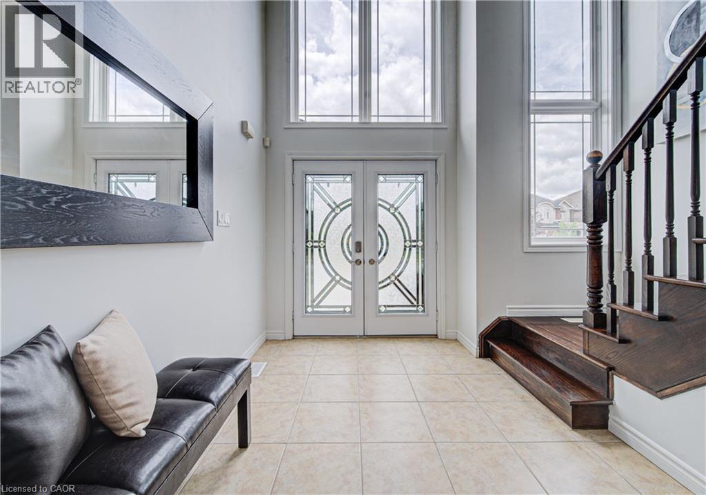 Two-story foyer featuring double entry doors with decorative glass, high transom windows, light-toned tiled flooring, and a dark wood staircase with spindle railing - 37 Davinci Boulevard, Hamilton, ON
