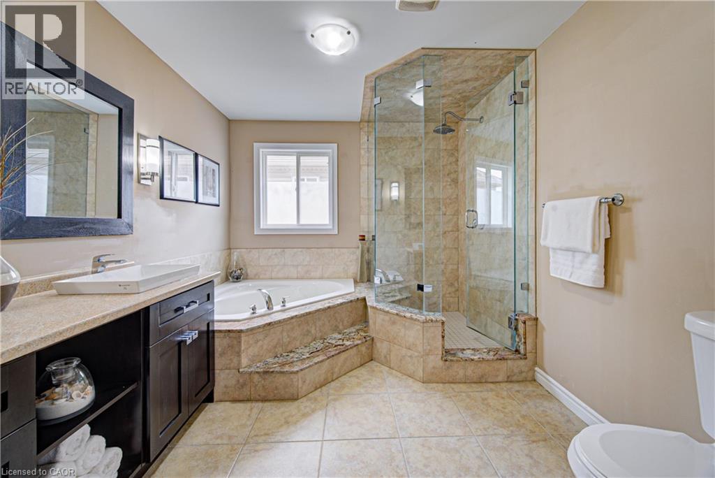Full bathroom featuring a glass-enclosed shower with tiled walls and a built-in bench, a corner soaking tub with tiled surround, a vanity with a vessel sink and dark wood-finish cabinetry, and tiled f - 37 Davinci Boulevard, Hamilton, ON