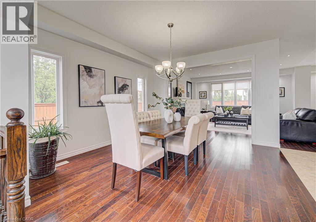 Dining area featuring wood-finish flooring, a tiered chandelier, and an open doorway to a living space with large windows - 37 Davinci Boulevard, Hamilton, ON