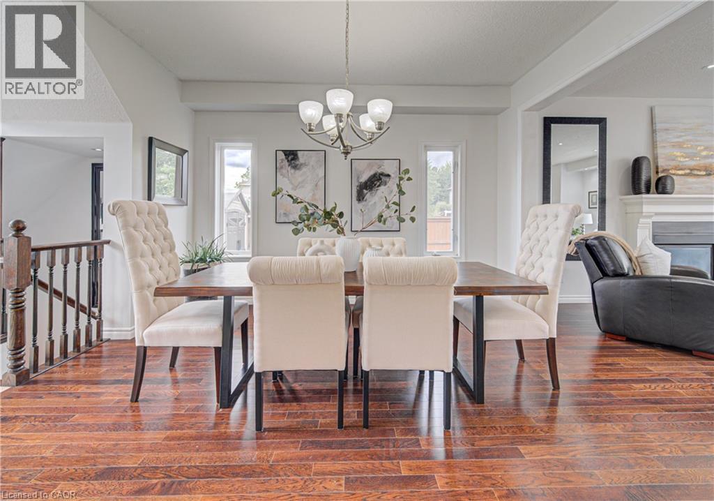 Spacious dining area featuring wood-finish flooring, a contemporary chandelier, and three distinct window panels - 37 Davinci Boulevard, Hamilton, ON