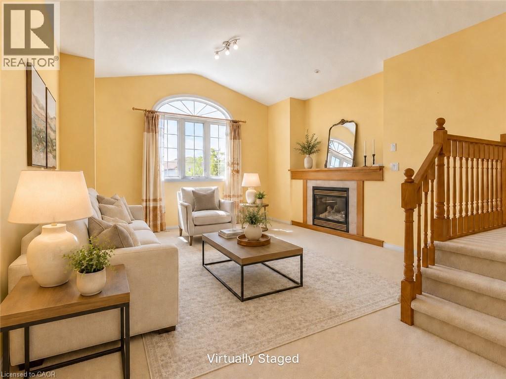 Living area featuring vaulted ceilings, a large arched window, a fireplace with a wood mantel, and carpeted stairs with wood railing - 212 Sleaford Street, Waterloo, ON