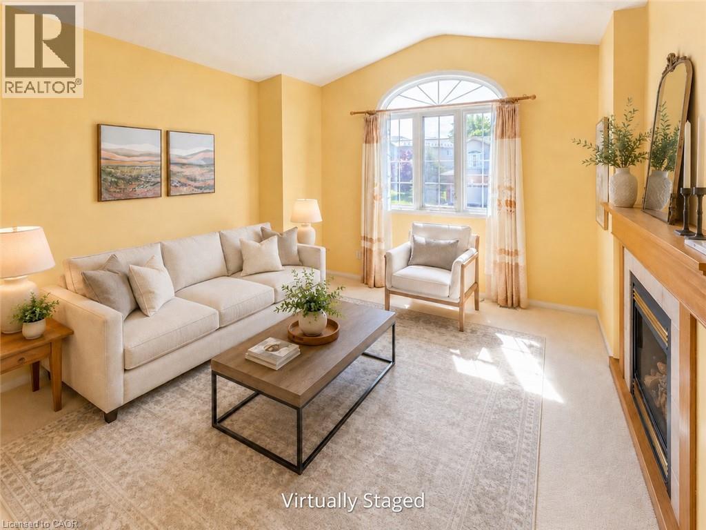 Spacious living area featuring a prominent arched window, a fireplace with a wood mantle, and soft carpeting - 212 Sleaford Street, Waterloo, ON
