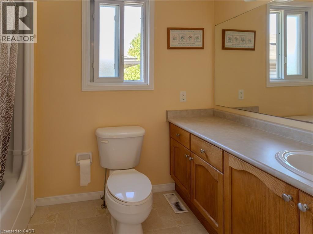 Bathroom featuring a single window, a built-in wood-finish vanity with a single basin, a full-width mirror, a white toilet, and tiled flooring - 212 Sleaford Street, Waterloo, ON