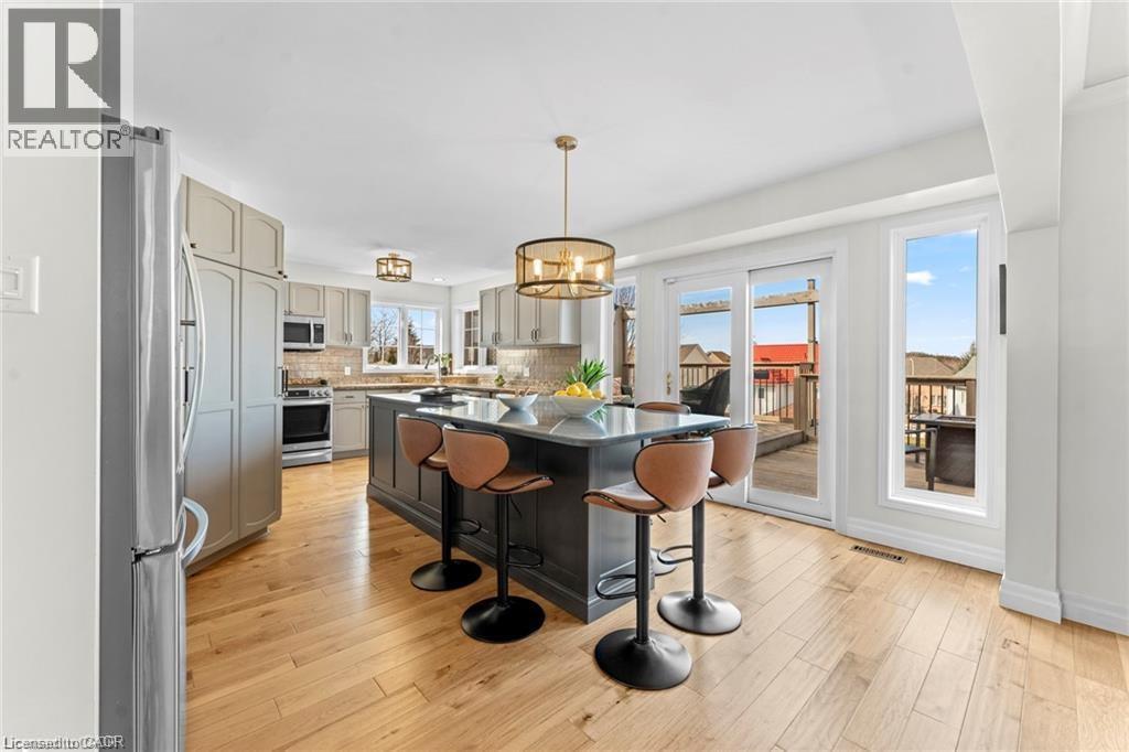 Kitchen featuring a dark-toned island with seating, stainless steel appliances, light wood-finish flooring, and direct access to an outdoor deck through sliding glass doors - 26 Shadyridge Place, Kitchener, ON