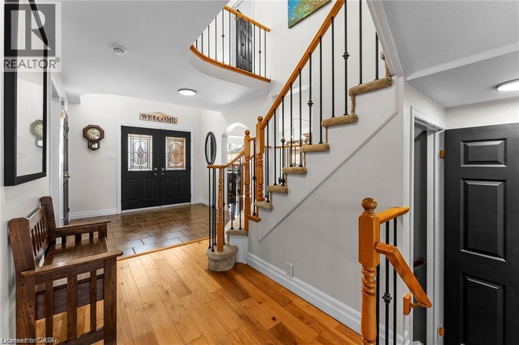 Two-story foyer featuring hardwood flooring, a contrasting tile entry, double doors with decorative glass inserts, a carpeted staircase with wood handrails and wrought iron balusters, and a second-sto - 26 Shadyridge Place, Kitchener, ON