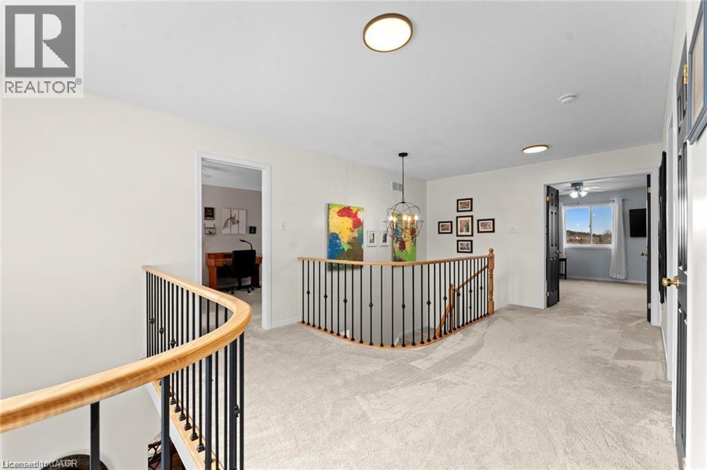 Carpeted upper-level hallway featuring a curved wood and iron railing, a chandelier, and multiple flush-mount ceiling lights - 26 Shadyridge Place, Kitchener, ON