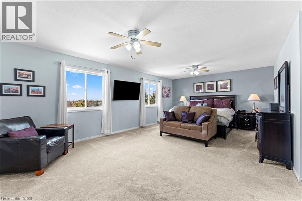 Spacious room with light neutral carpeting, multiple windows providing natural light, and two ceiling fans - 26 Shadyridge Place, Kitchener, ON