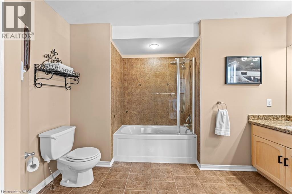 Bathroom featuring a tub and shower combination with glass enclosure, a vanity with a granite-style countertop, light wood cabinetry, and a white toilet - 26 Shadyridge Place, Kitchener, ON