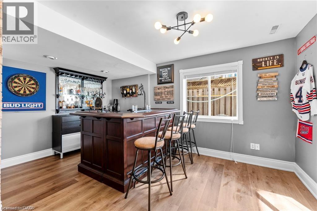 Built-in dark wood bar with seating for four, featuring an integrated glass rack and adjacent cabinetry - 26 Shadyridge Place, Kitchener, ON