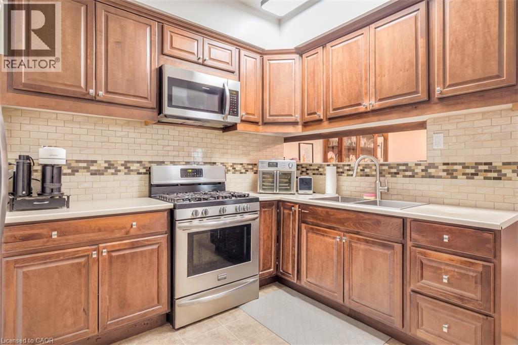 Kitchen featuring stainless steel appliances, wood cabinetry, light countertops, and a subway tile backsplash with decorative mosaic - 41 Springhurst Avenue, Toronto, ON