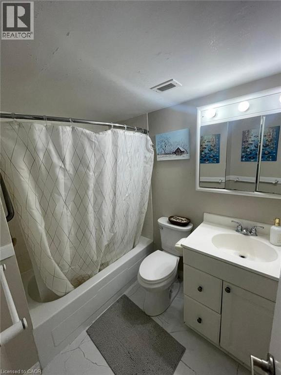 White vanity with chrome fixtures and integrated sink, alongside a white toilet and a bathtub with shower - 225 Harvard Place Unit# 1505, Waterloo, ON