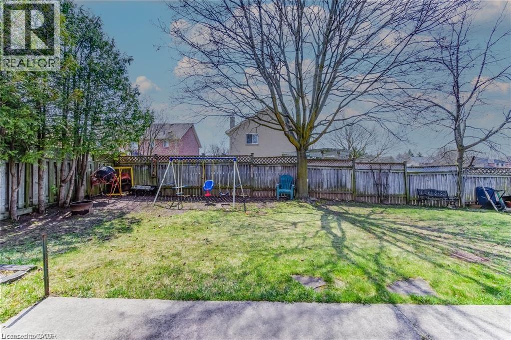 Expansive grassy yard featuring mature trees and a wooden privacy fence - 27 Tassie Lane, Cambridge, ON