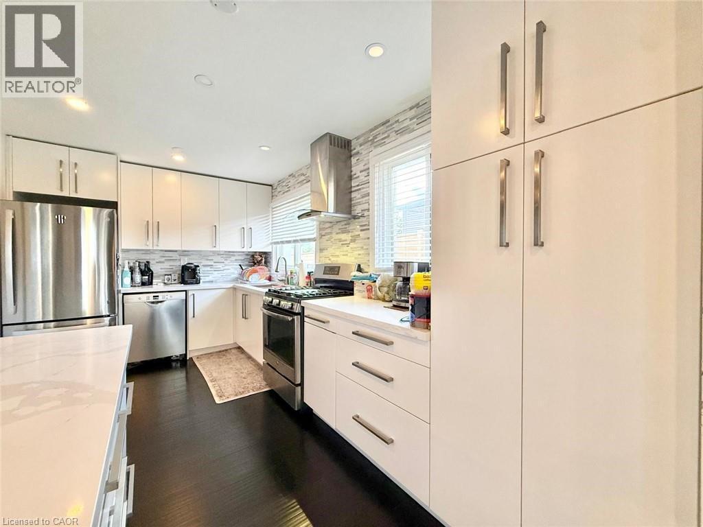 Modern kitchen featuring white cabinetry, dark wood-finish flooring, stainless steel appliances, a stacked tile backsplash, and recessed lighting - 3135 Palmer Drive, Burlington, ON