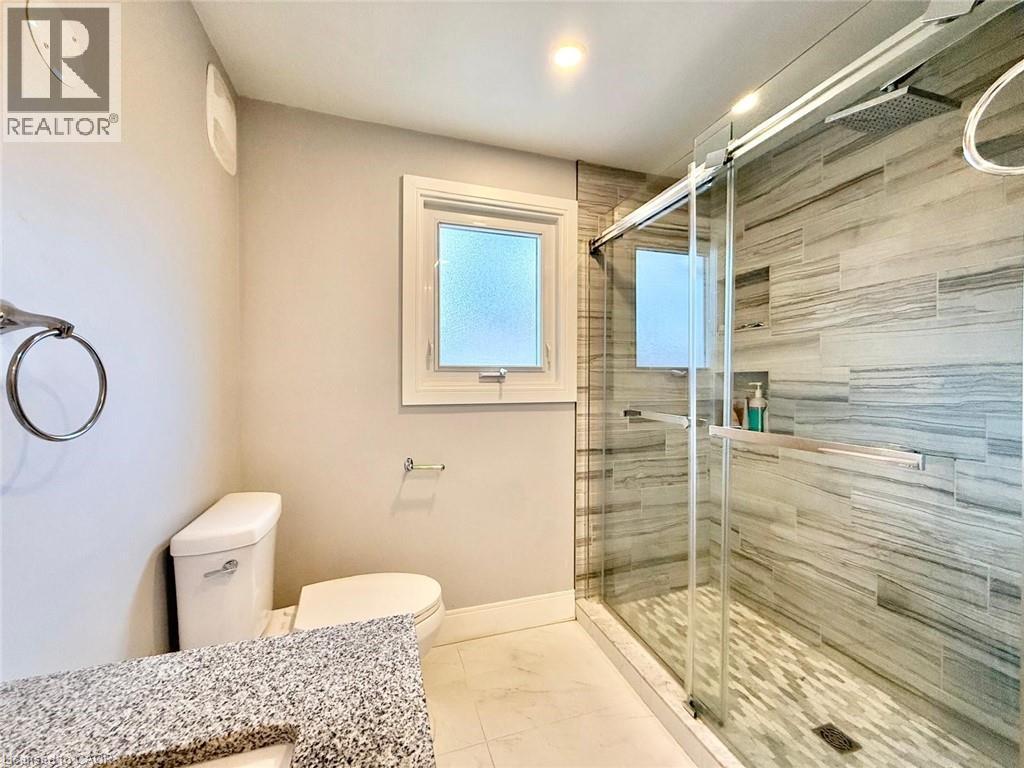 Three-quarter bathroom featuring a granite-finish vanity, white toilet, and a glass-enclosed shower - 3135 Palmer Drive, Burlington, ON