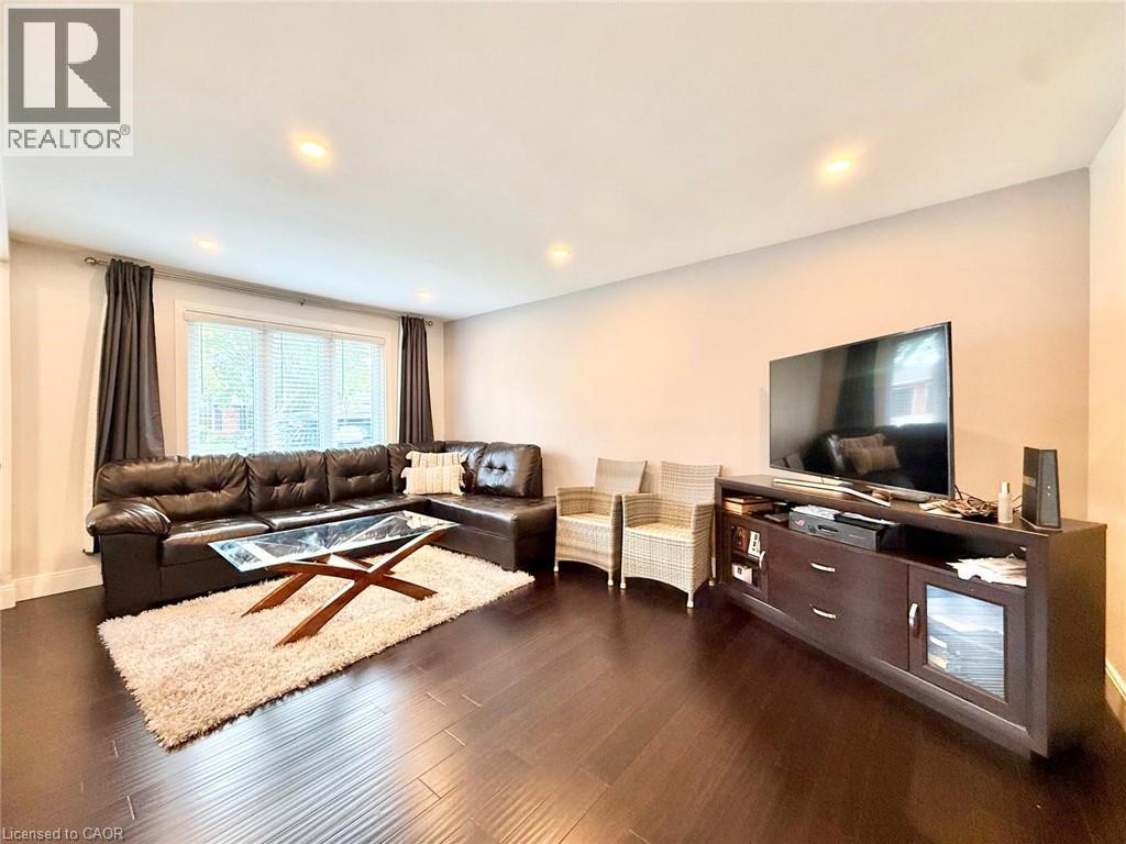 Spacious living area featuring dark wood-finish flooring, recessed lighting, and a large window with blinds - 3135 Palmer Drive, Burlington, ON