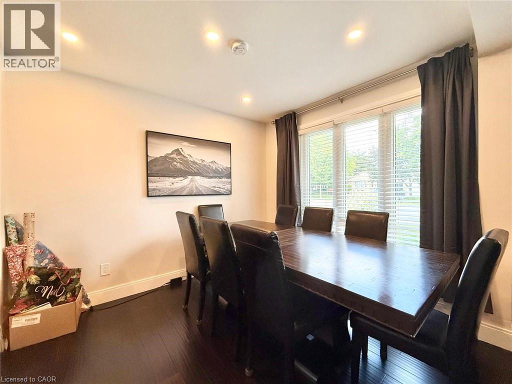 Dining area featuring dark wood-finish flooring, recessed lighting, and a wide window with blinds and dark drapery panels - 3135 Palmer Drive, Burlington, ON
