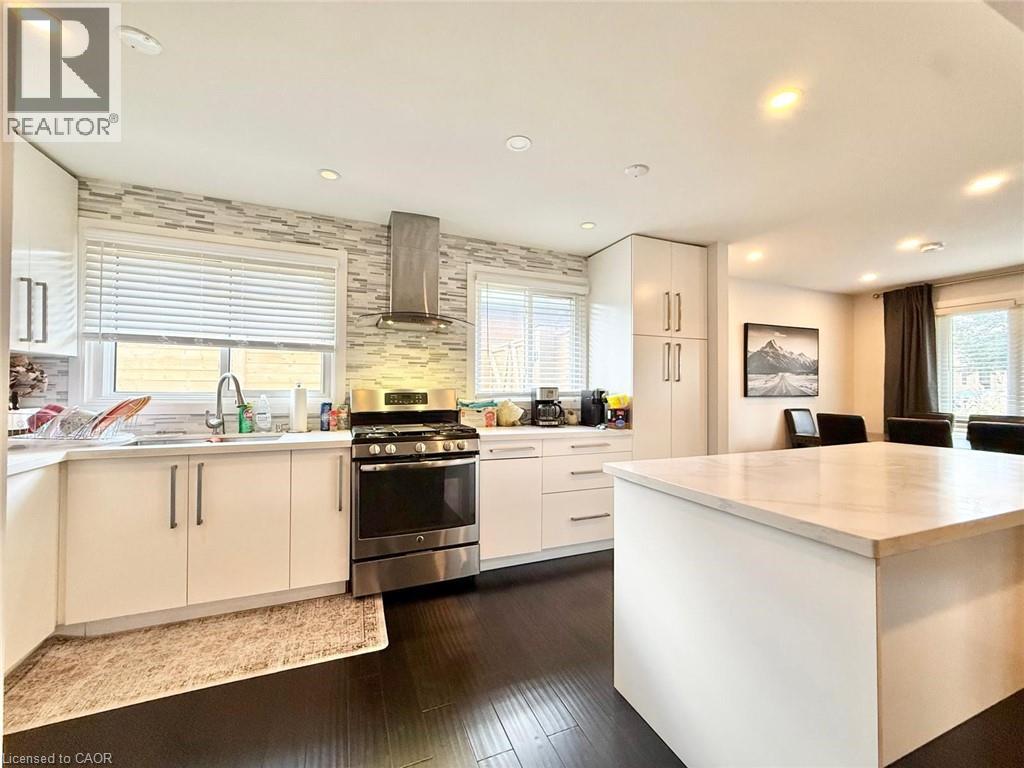 Contemporary kitchen featuring dark wood-finish flooring, white cabinetry, and a large island with a light-toned countertop - 3135 Palmer Drive, Burlington, ON