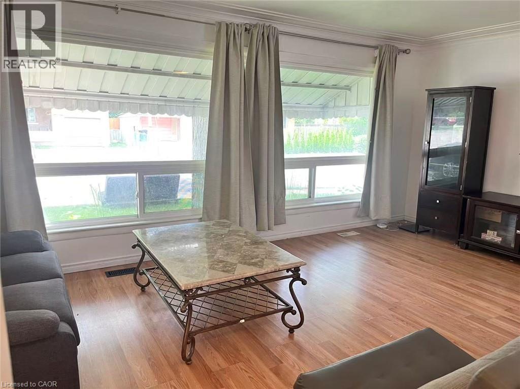 Bright living area featuring expansive windows, wood-finish flooring, a built-in display cabinet, and crown molding - 110 Peppler Street, Waterloo, ON