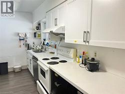 Kitchen featuring white shaker-style cabinetry with brushed nickel hardware, white stone-finish countertops, stainless steel sink, and wood-finish flooring -