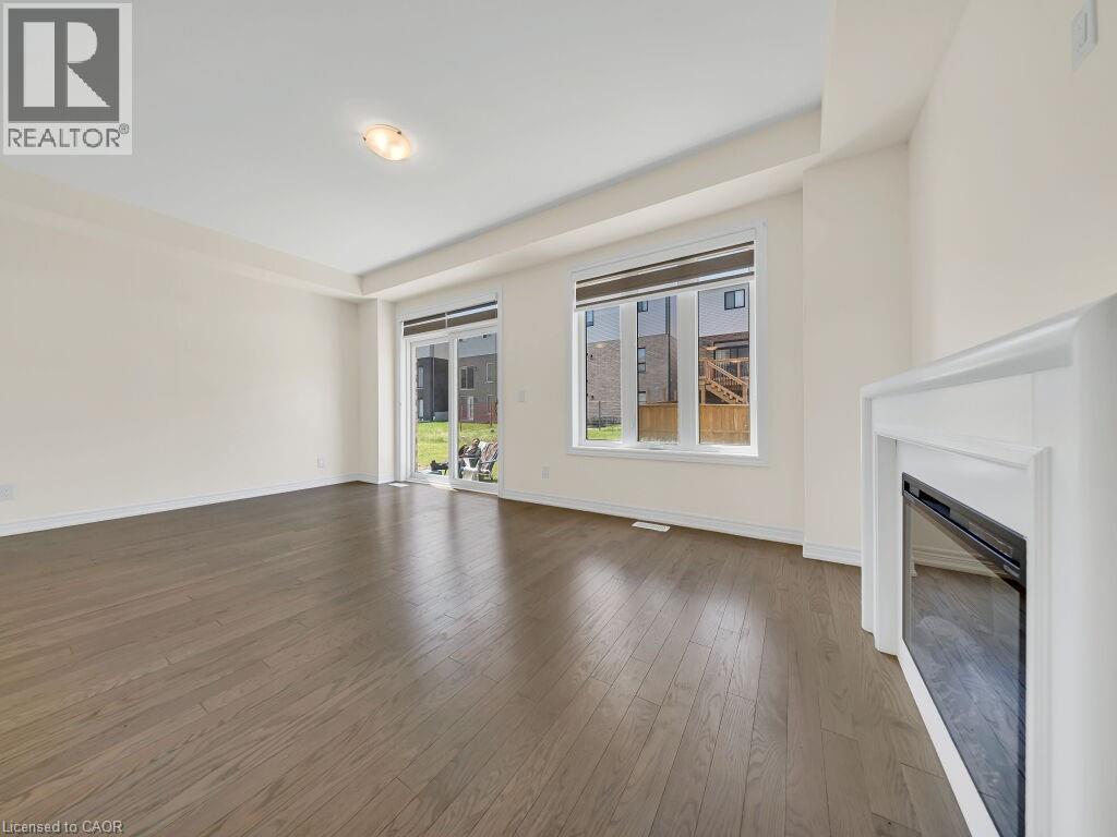 Spacious room featuring wood-finish flooring, a contemporary electric fireplace, and abundant natural light from a large window and sliding glass door - 76 Grassbourne Avenue, Kitchener, ON