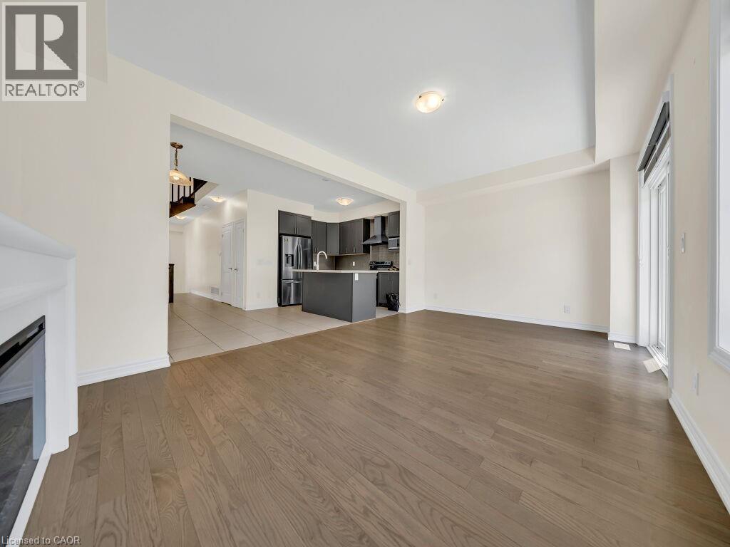Spacious room featuring wood-finish flooring, a built-in fireplace, and abundant natural light from a large window - 76 Grassbourne Avenue, Kitchener, ON