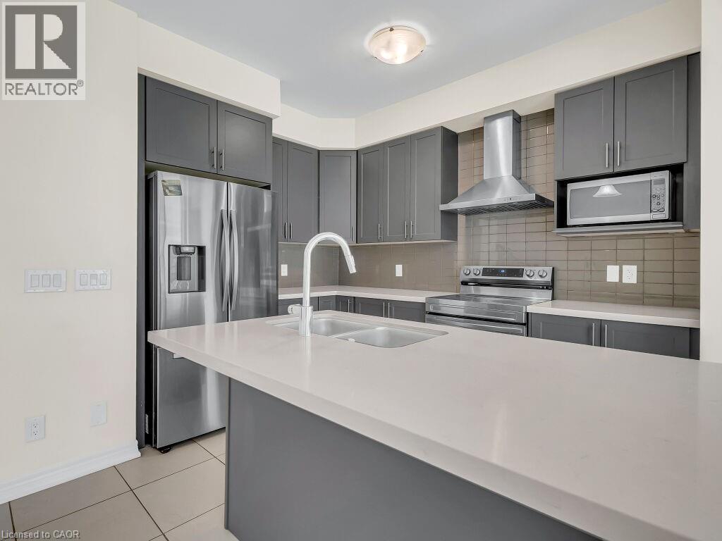 Modern kitchen featuring gray cabinetry, stainless steel appliances, a white single-basin sink with a gooseneck faucet, light-toned countertops, and a tiled backsplash - 76 Grassbourne Avenue, Kitchener, ON