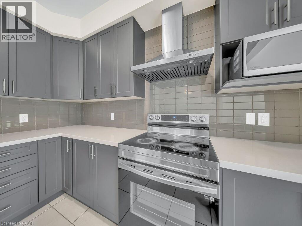 Contemporary kitchen featuring gray shaker-style cabinetry, light-toned countertops, a stainless steel range with a matching range hood, and a built-in microwave - 76 Grassbourne Avenue, Kitchener, ON
