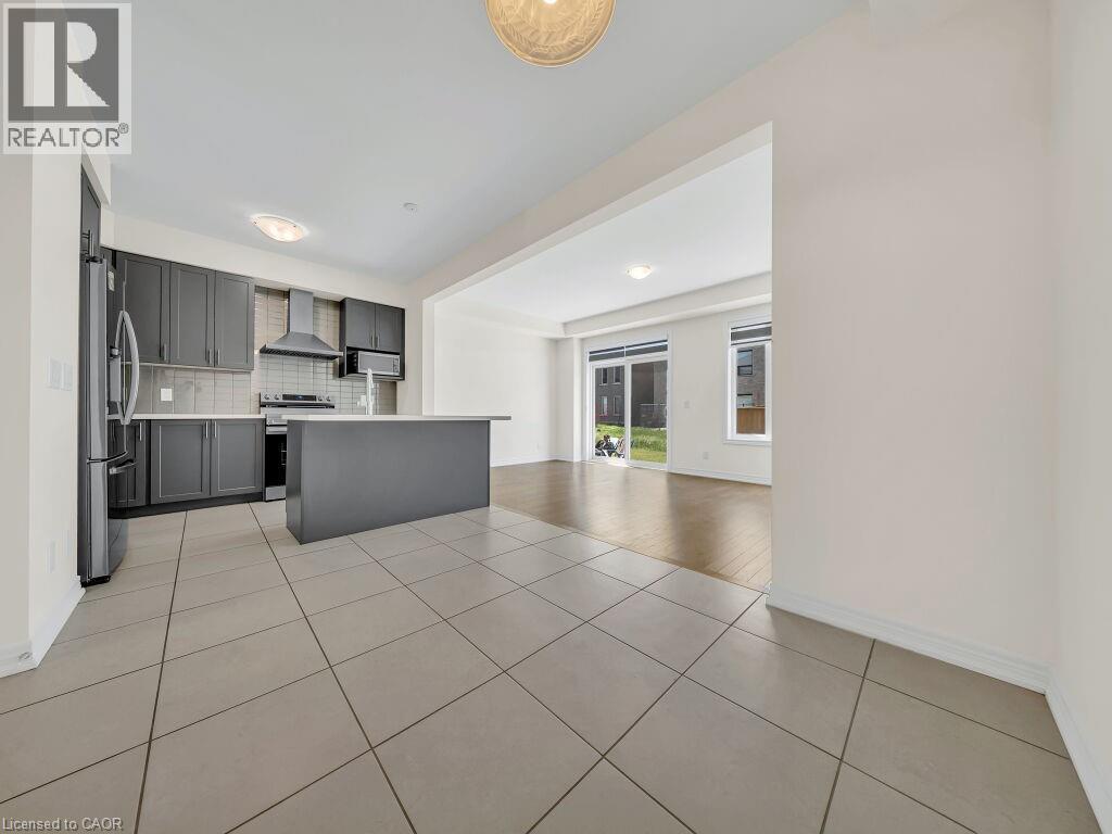 Modern kitchen featuring dark cabinetry, stainless steel appliances, a center island, and tiled flooring - 76 Grassbourne Avenue, Kitchener, ON