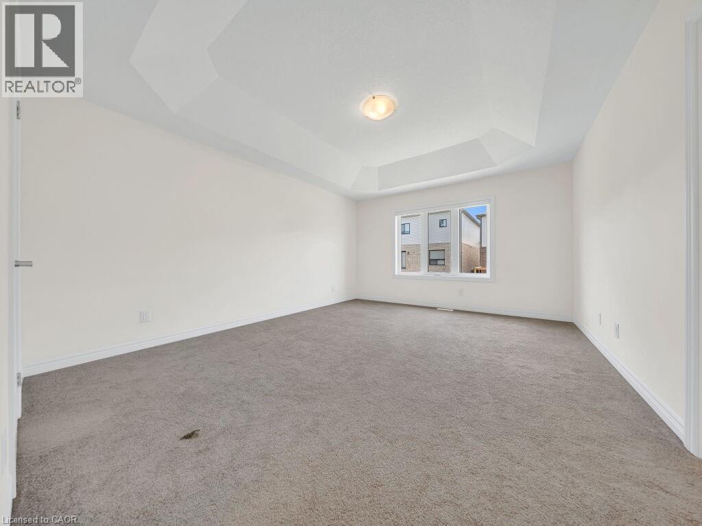 Spacious room featuring a tray ceiling, flush-mount lighting, broad baseboards, gray carpet, and a multi-pane window - 76 Grassbourne Avenue, Kitchener, ON