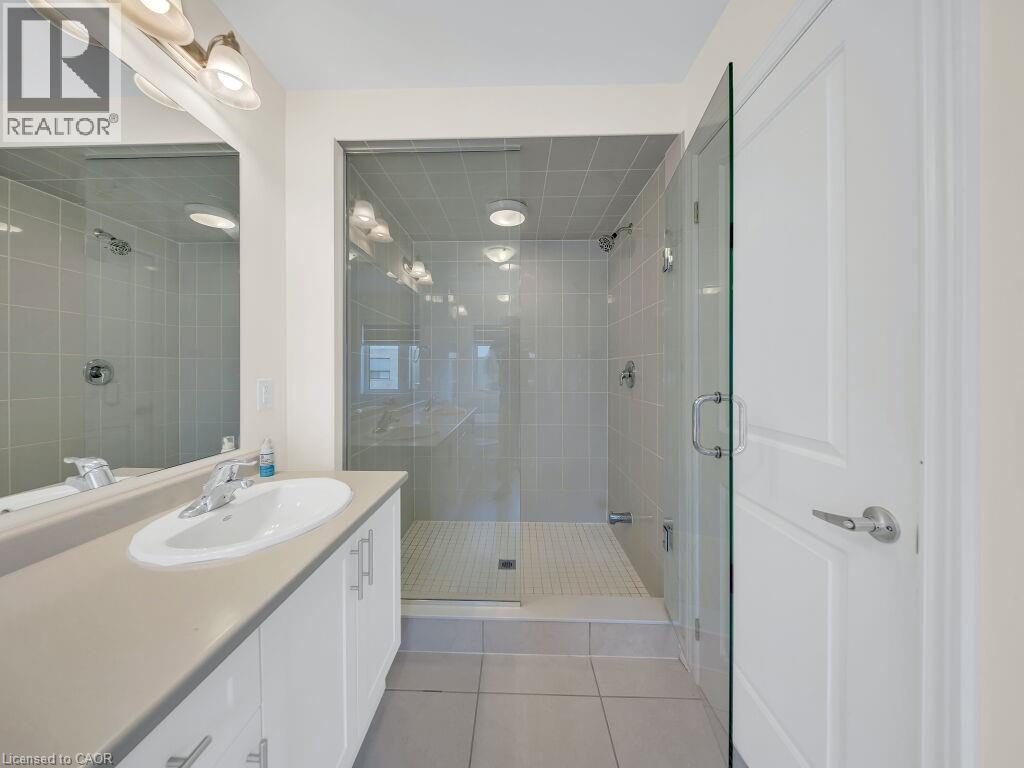 Bathroom featuring a glass-enclosed shower with tile surround, a single vanity with a neutral countertop, white cabinetry with silver-tone hardware, and a large wall mirror - 76 Grassbourne Avenue, Kitchener, ON