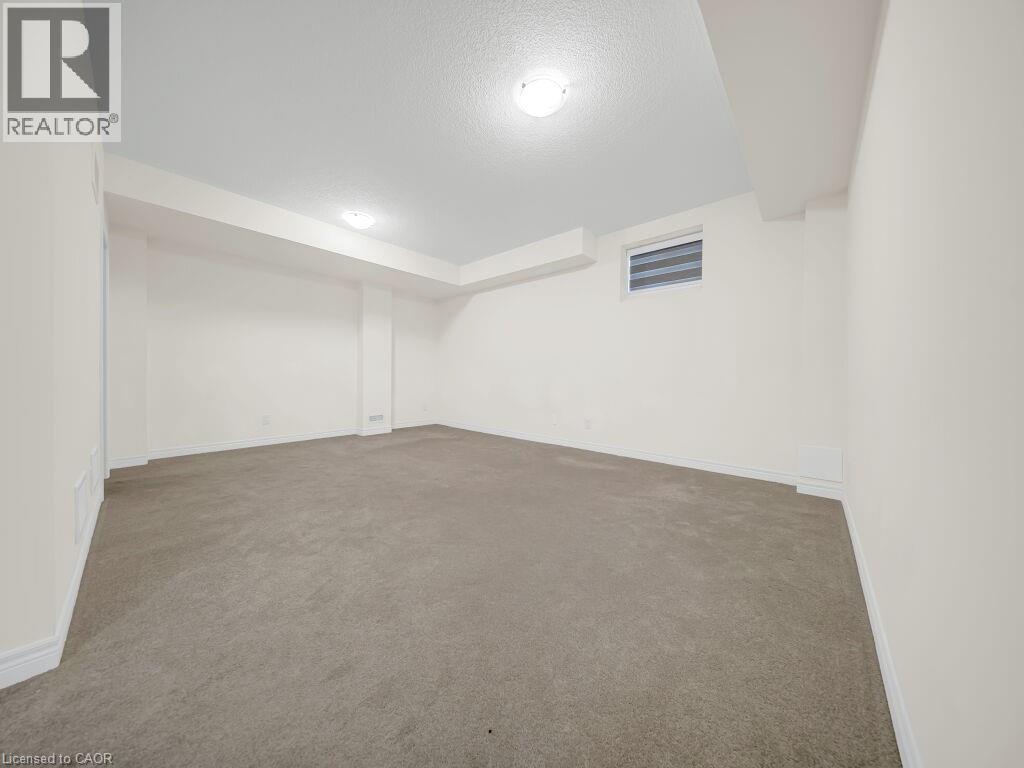 Spacious room with light-toned wall-to-wall carpeting and neutral white walls - 76 Grassbourne Avenue, Kitchener, ON