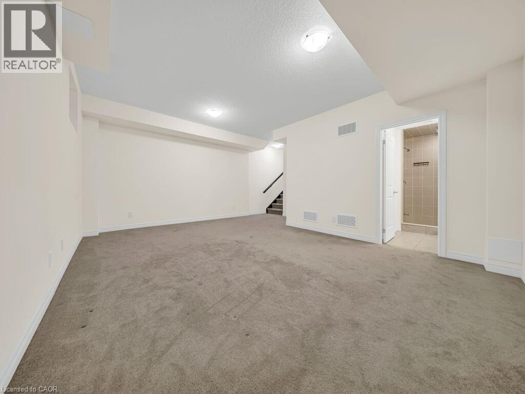 Expansive carpeted room featuring recessed lighting, a staircase with dark railings, and a doorway leading to a tiled shower enclosure - 76 Grassbourne Avenue, Kitchener, ON