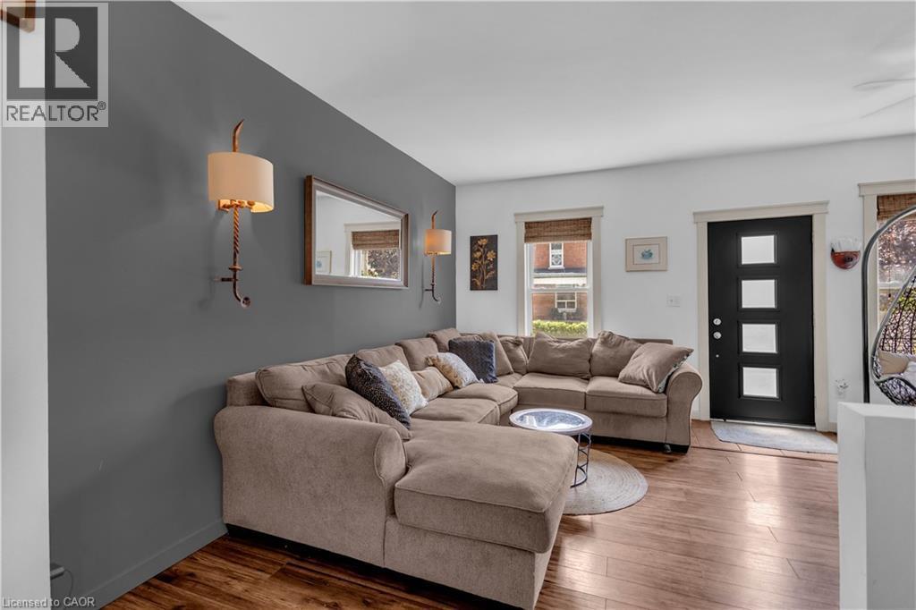 Open-concept living space featuring wood-finish flooring, a modern black entry door with frosted glass panels, and two windows with natural woven shades - 30 Sunset Avenue, Hamilton, ON