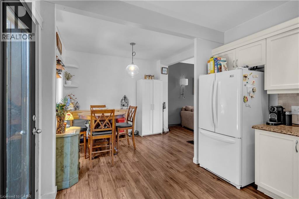 Open-concept living space featuring wood-finish flooring, white cabinetry with a stone-finish countertop, a clear glass pendant light, and a black-framed glass door - 30 Sunset Avenue, Hamilton, ON