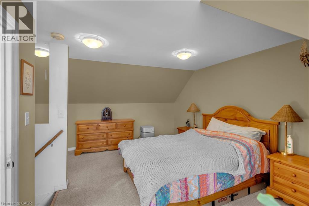 Carpeted bedroom featuring an angled ceiling, neutral wall paint, two ceiling-mounted dome lights, and a white interior door - 30 Sunset Avenue, Hamilton, ON