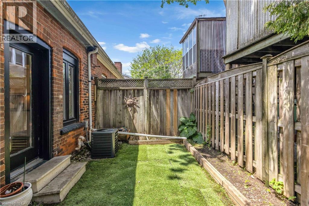 Private outdoor space featuring brick exterior, wood fencing, artificial turf, and a planting bed - 30 Sunset Avenue, Hamilton, ON