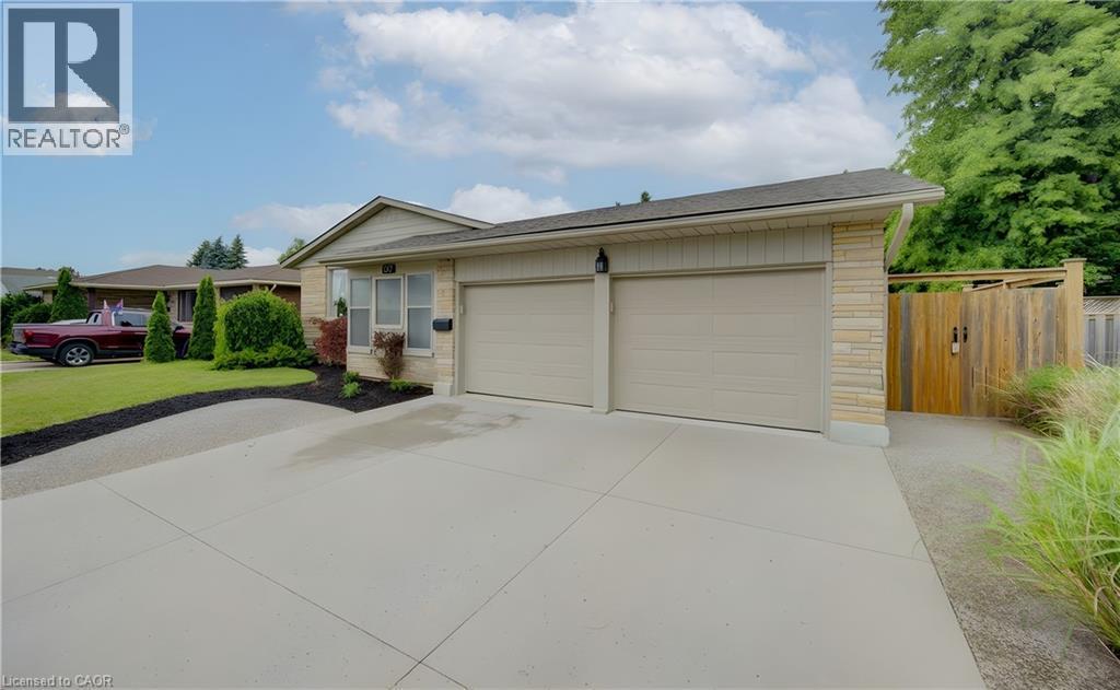 Single-story residence featuring a two-car garage with light-toned doors, stone veneer accents, light-colored siding, and a concrete driveway - 127 Strathcona Crescent, Kitchener, ON