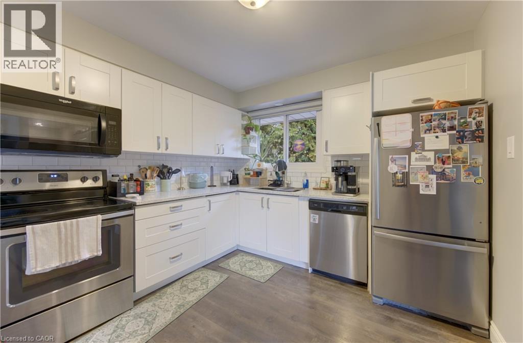 Kitchen featuring white shaker-style cabinetry, wood-finish flooring, stainless steel appliances, and a subway tile backsplash - 127 Strathcona Crescent, Kitchener, ON